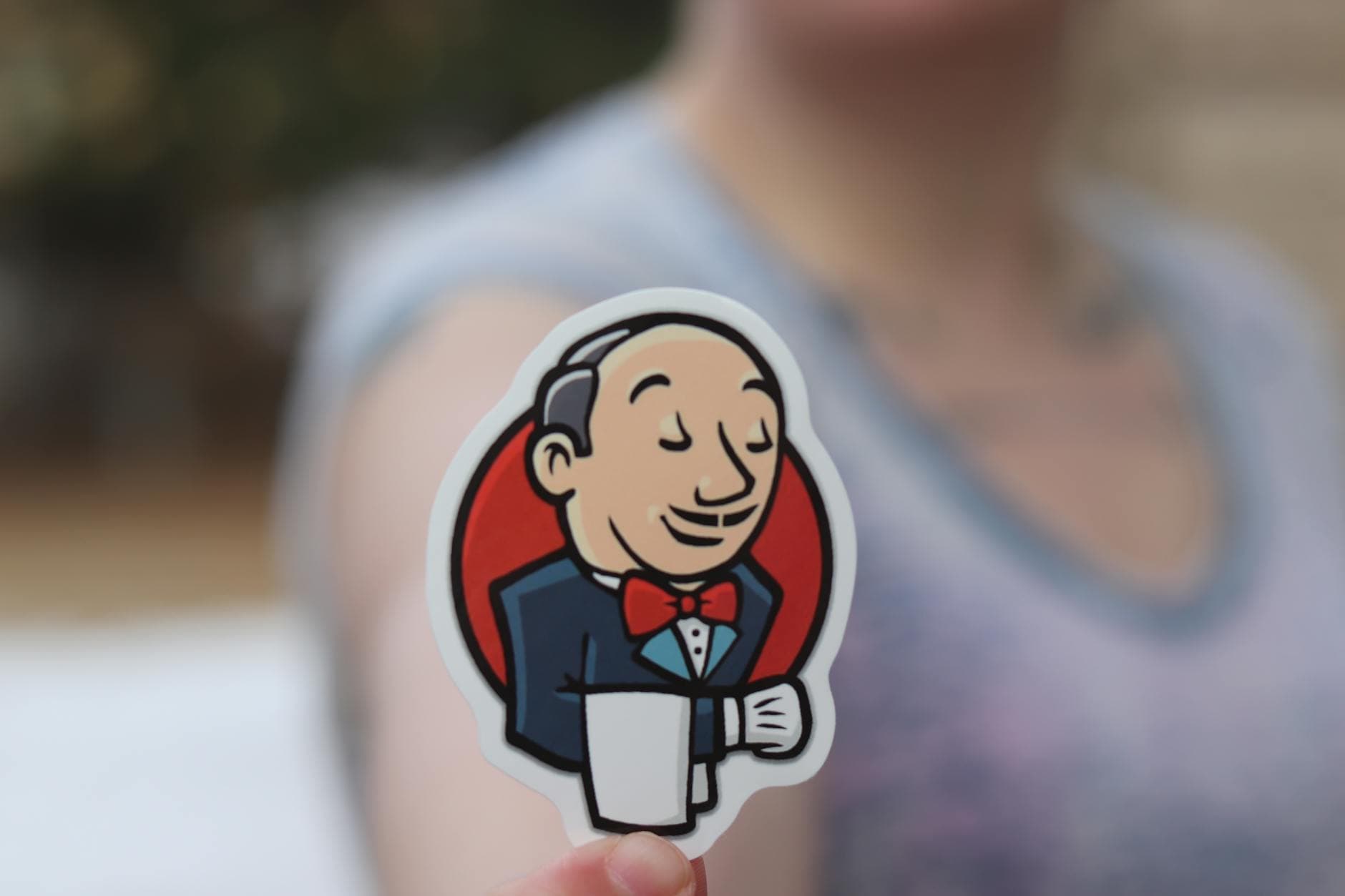 Hand holding a Jenkins sticker outdoors, blurred background for focus effect.