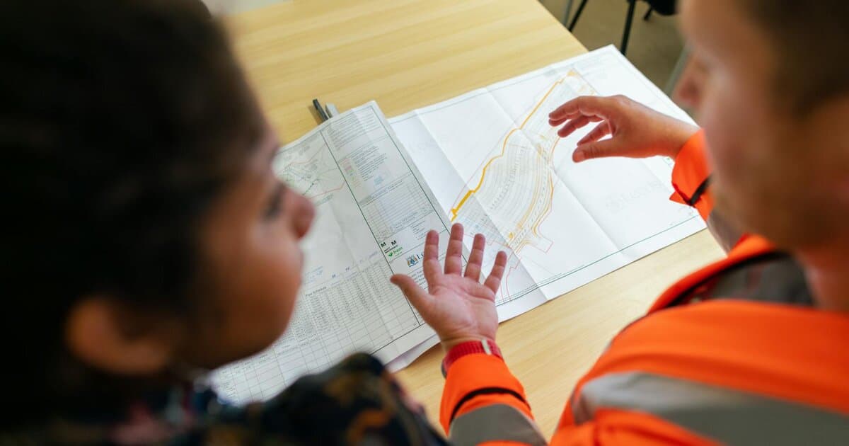 Two engineers reviewing construction blueprints on a table in an office setting.