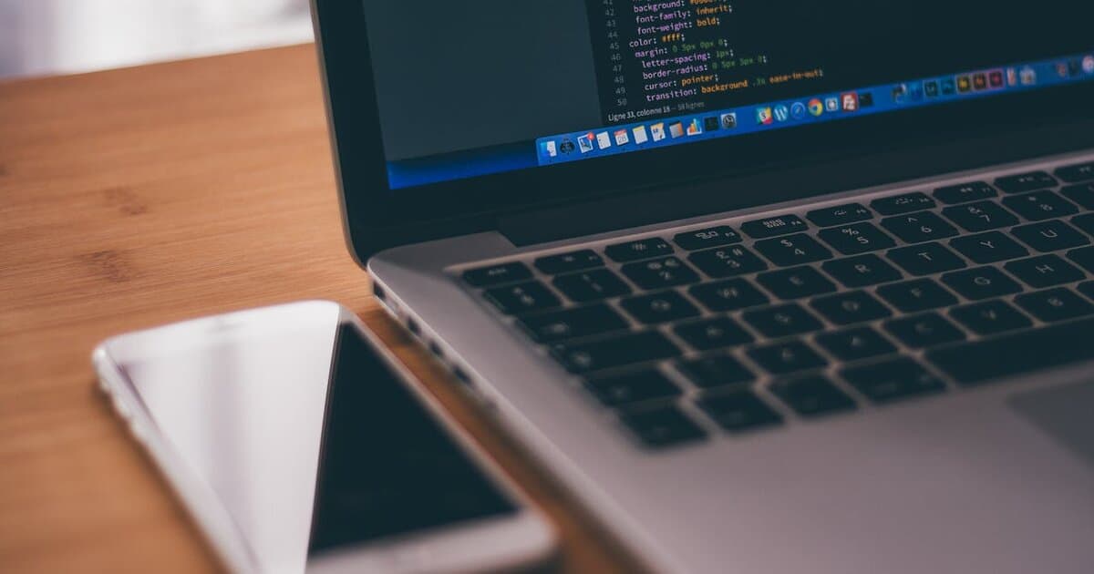 Laptop displaying code with smartphone on desk - mobile app development