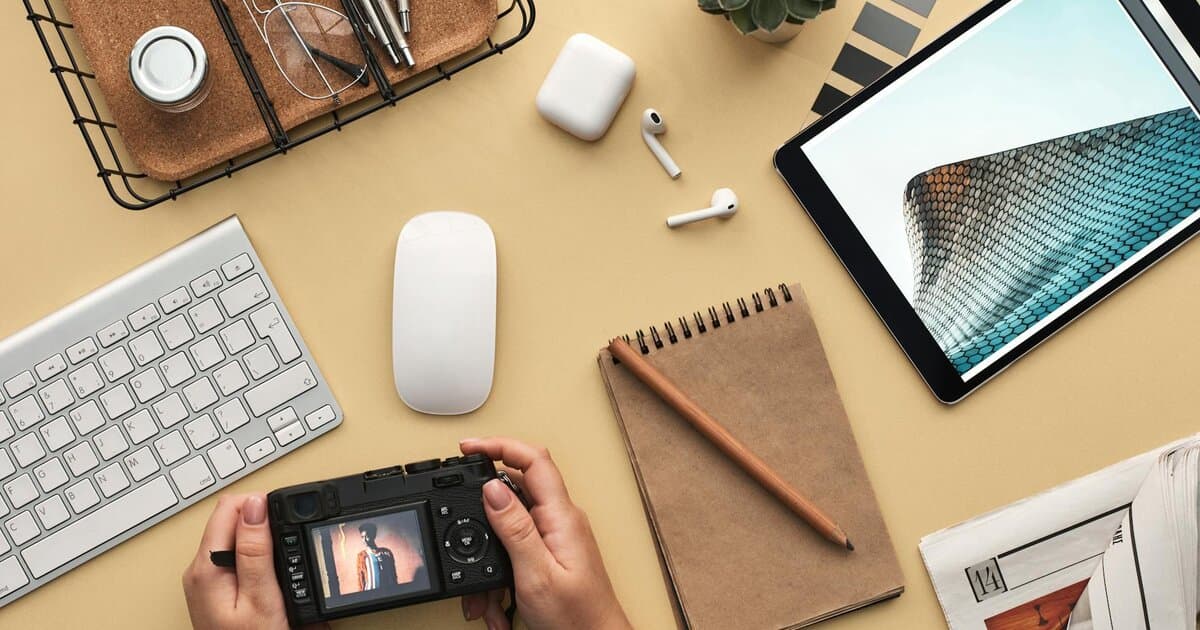 Overhead view of a modern workspace featuring tech gadgets, a camera, and a notepad.