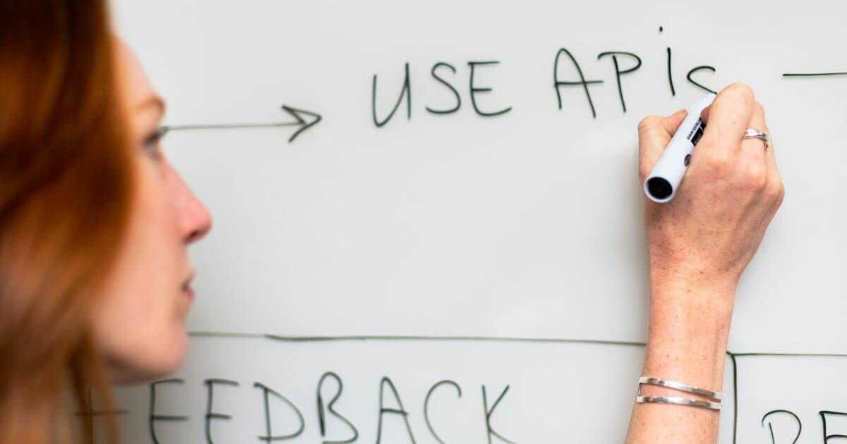 A woman writes 'Use APIs' on a whiteboard, focusing on software planning and strategy.