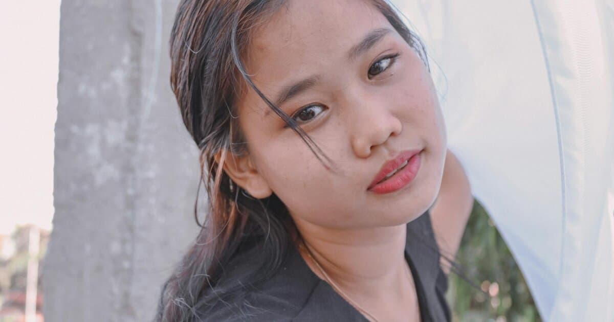A young woman stands outdoors, drying fabric under natural daylight. Captured with Canon EOS 1500D.