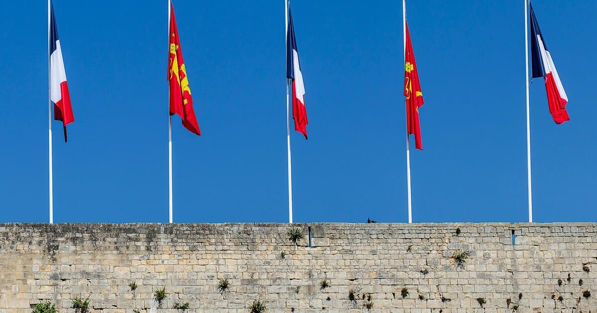 French and Normandy flags on poles above ancient wall in Caen, Normandy, France.