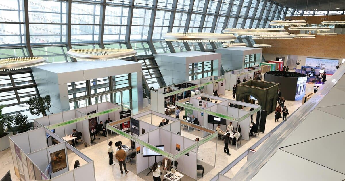 A bustling trade show exhibition inside a modern hall with people networking and exploring booths.