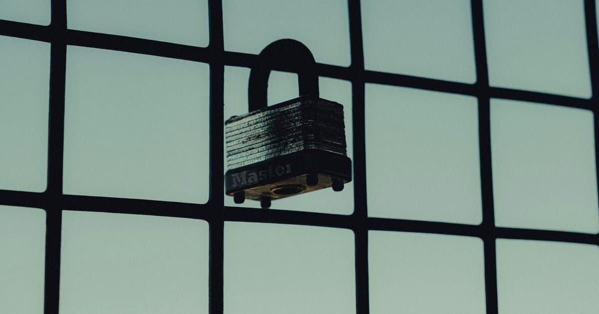 Close-up of a steel padlock on a mesh fence, symbolizing protection and security.