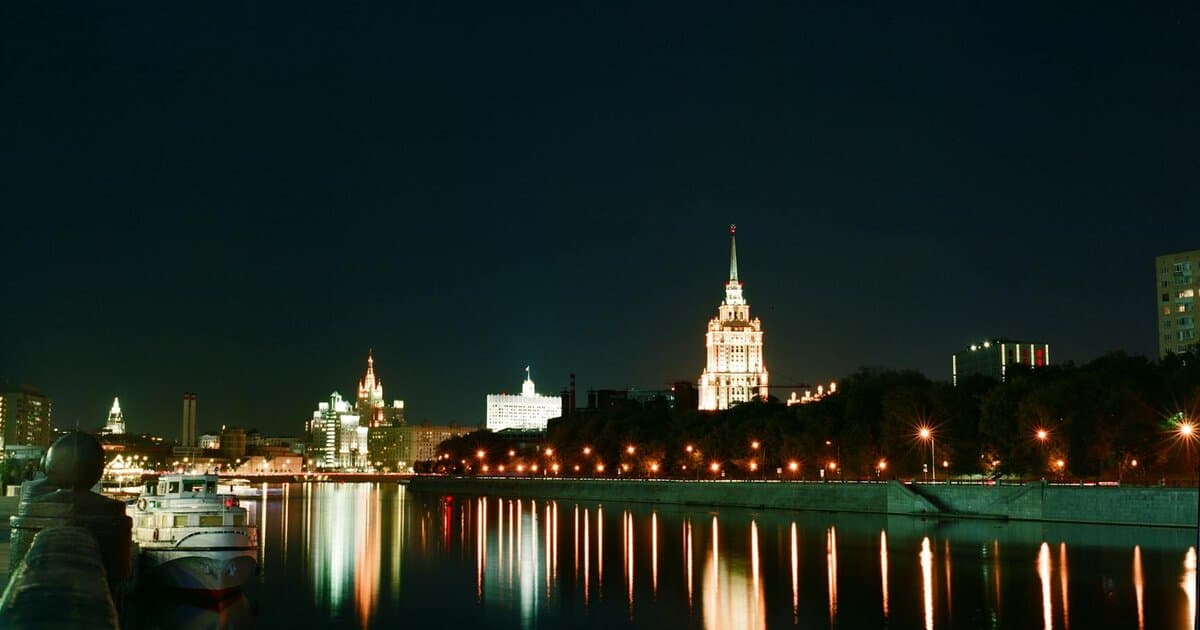 Cityscape at night with illuminated buildings and reflections on the river, creating a scenic view.