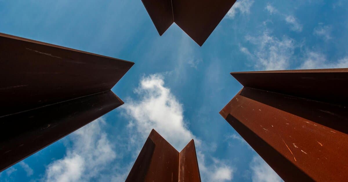 Artistic angle of metal beams creating a unique pattern against the blue sky and clouds.