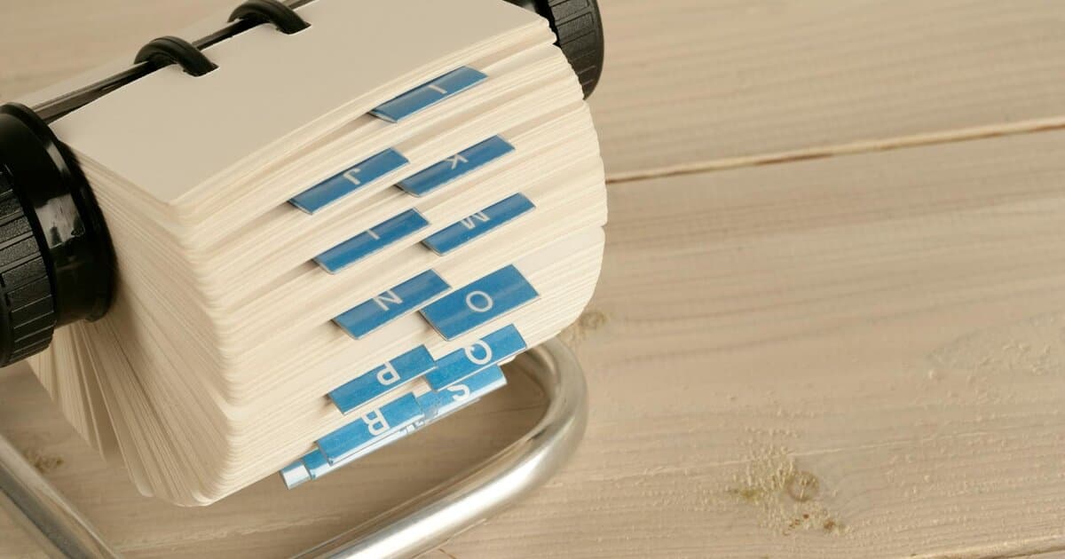 A close-up of a traditional Rolodex with alphabet tabs on a wooden desk.