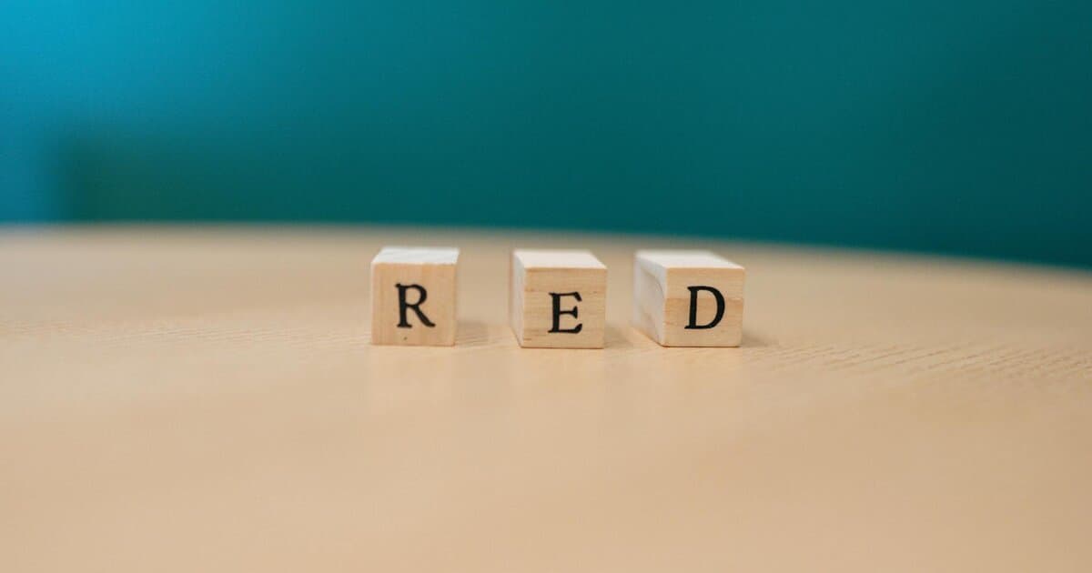 Close-up of wooden blocks spelling 'RED' on a table with teal background.