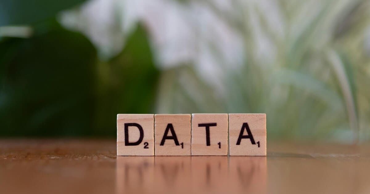 Scrabble tiles spelling 'DATA' on a wooden table with a blurred plant background.