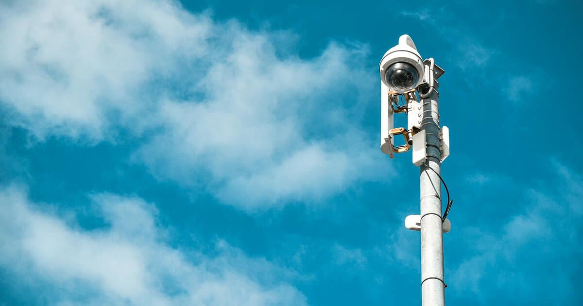 Close-up of a surveillance camera on a pole under a clear blue sky.