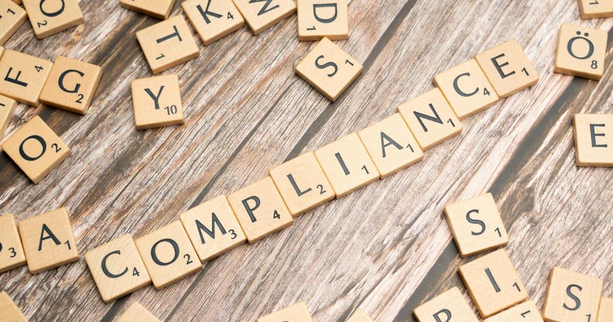 Wooden letter tiles forming the word 'COMPLIANCE' on a rustic wooden background.
