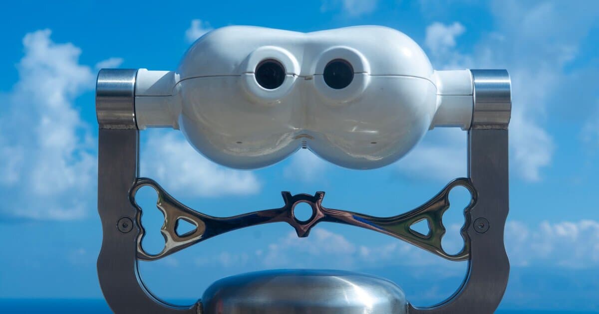 View through coin-operated binoculars with a clear blue sky and ocean horizon.