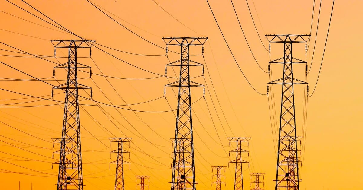Silhouetted power lines against a vibrant orange sunset, symbolizing energy and infrastructure.