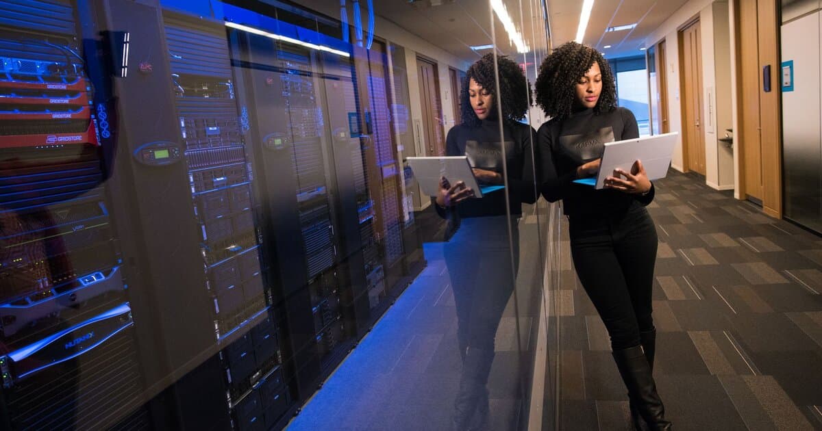 A woman using a laptop navigating a contemporary data center with mirrored servers.