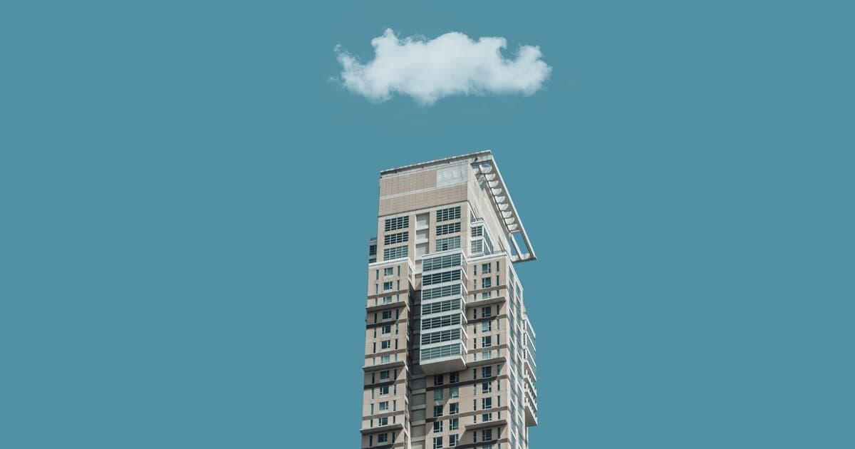 Low-angle shot of a modern high-rise building against a clear sky with a single cloud above.