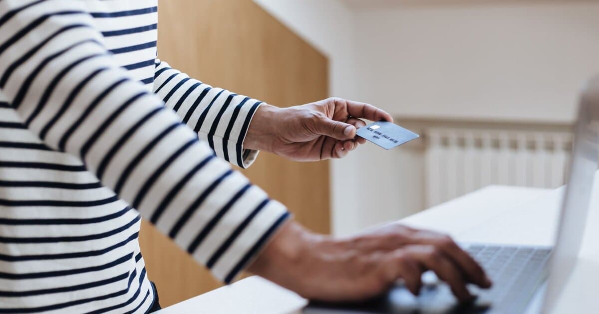 Person using a credit card for online shopping on a laptop indoors.