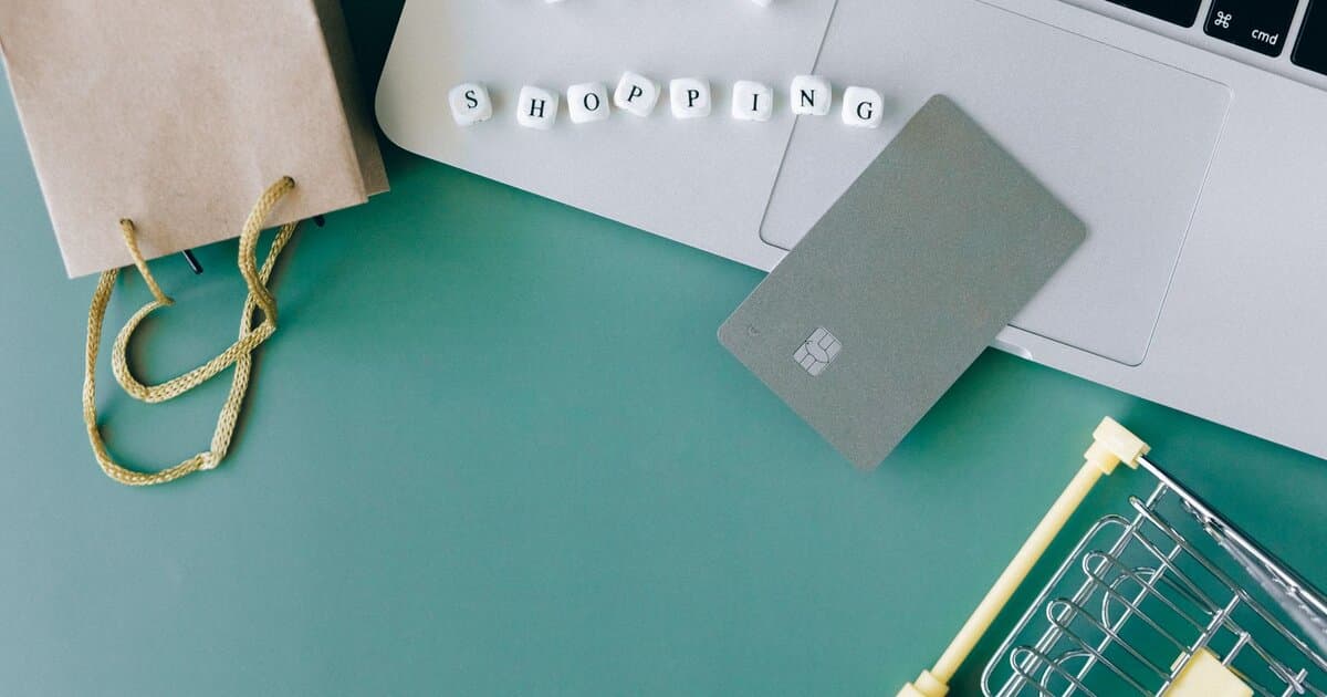 Flat lay of online shopping essentials with laptop, card, and shopping cart.