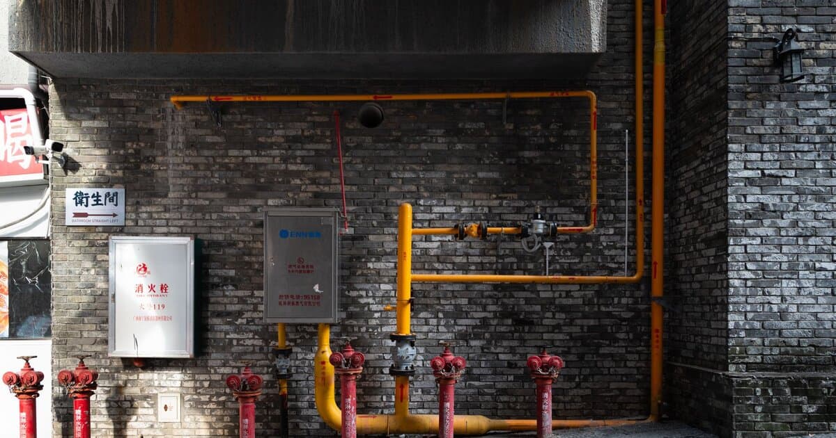 Brick wall with red hydrants and yellow piping in an urban alleyway setting.
