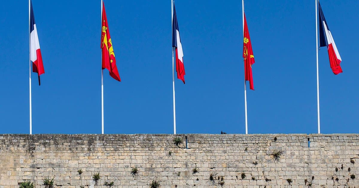 French and Normandy flags on poles above ancient wall in Caen, Normandy, France.
