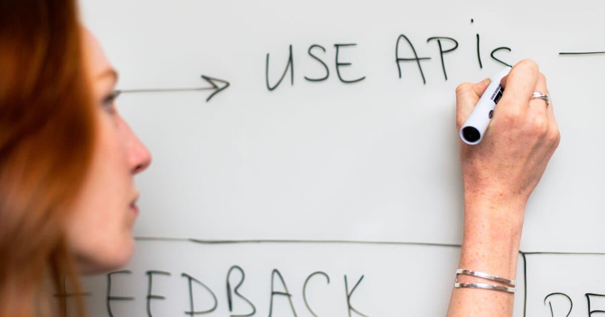 A woman writes 'Use APIs' on a whiteboard, focusing on software planning and strategy.