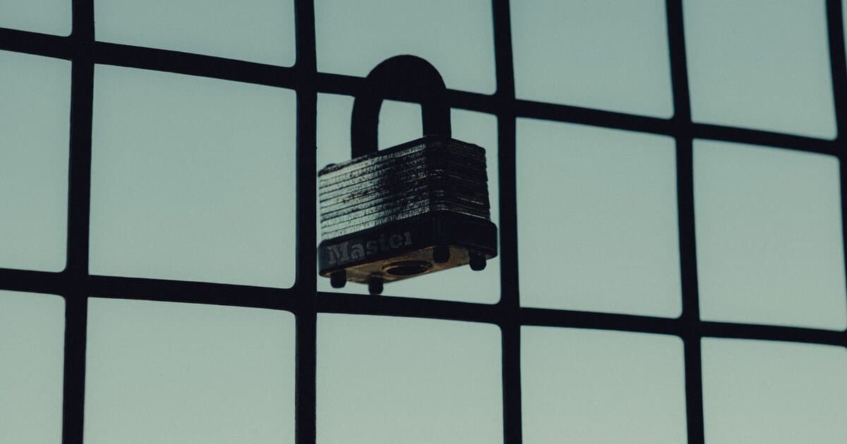 Close-up of a steel padlock on a mesh fence, symbolizing protection and security.