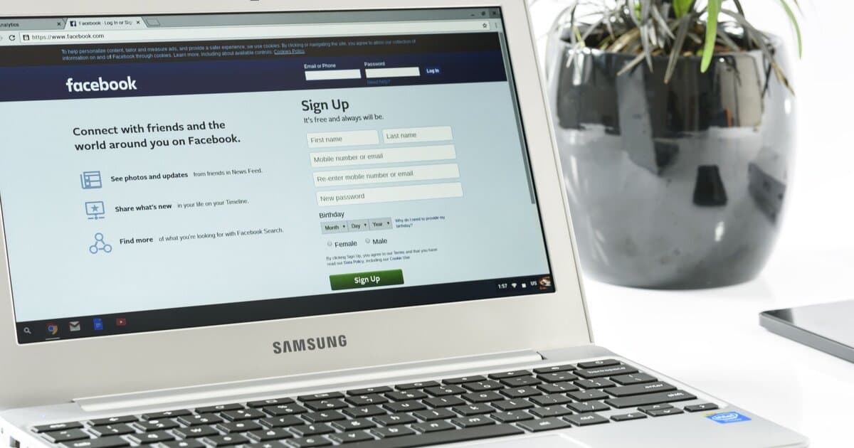 Open Samsung laptop showing Facebook sign-up page next to a potted plant. Ideal for technology themes.