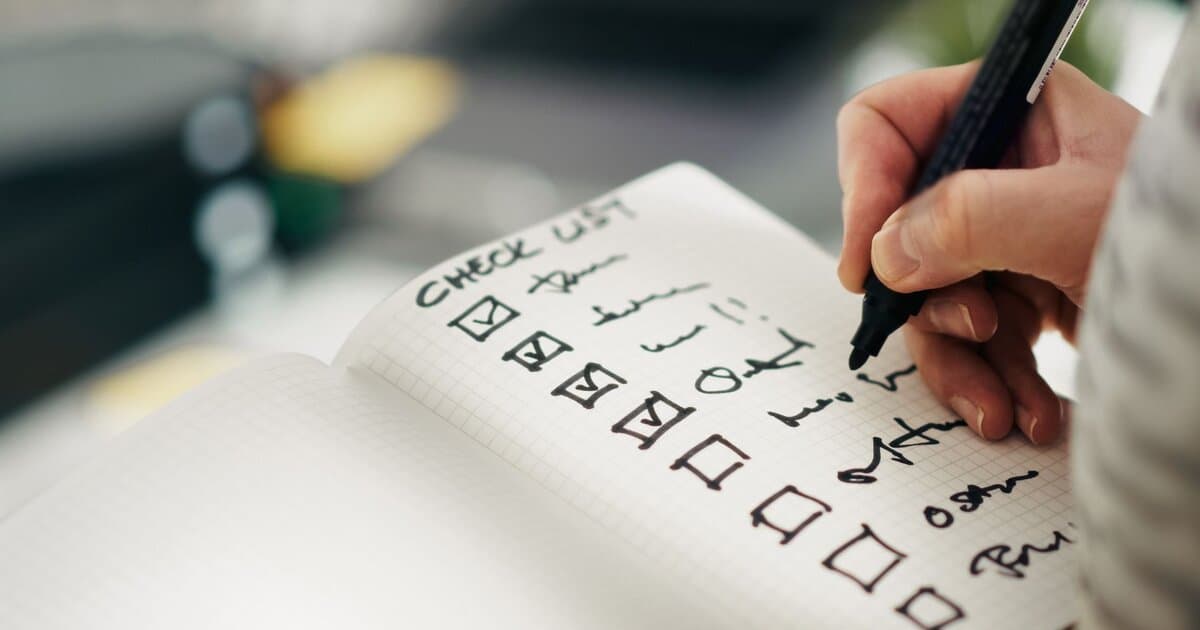 Hand writing tasks on a checklist, emphasizing productivity and organization.