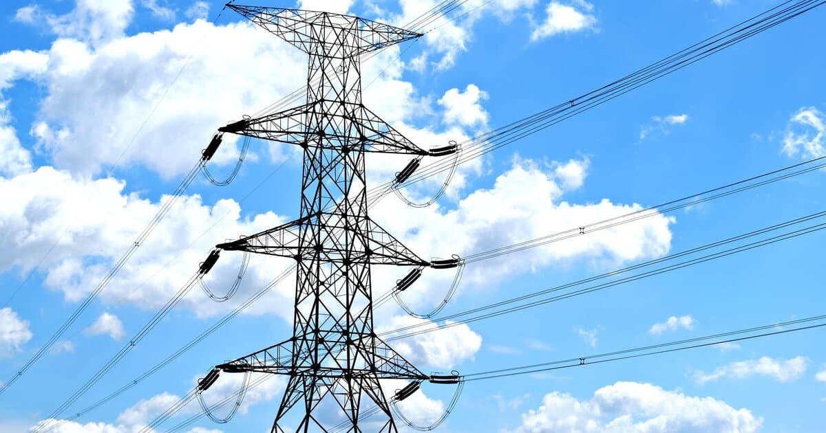 Electricity pylon with high voltage lines set against a vibrant blue sky with clouds.