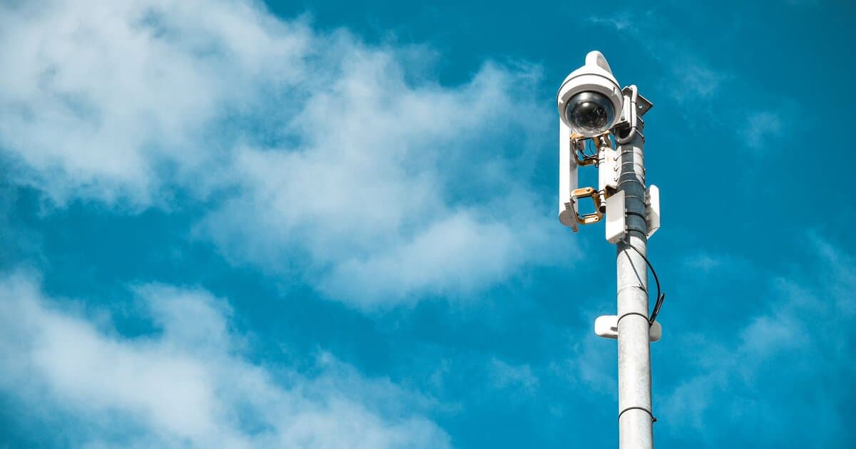 Close-up of a surveillance camera on a pole under a clear blue sky.